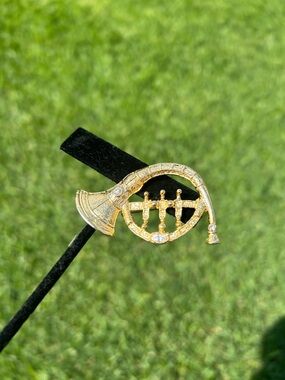 Gold-tone brooch shaped like a French horn, featuring rhinestone accents.